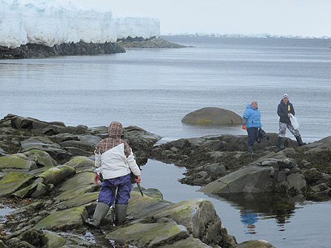 Quatre personnes se trouvent au-dessus d’une banquise près d’une grande étendue d’eau, avec des rivages rocheux en contrebas. L’une d’elles manie une corde. Toutes sont vêtues d’habits d’hiver.